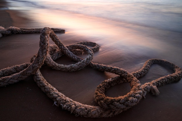 Foto corda de barco velha na praia durante o nascer do sol