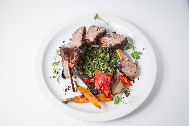 Cordero al horno con zanahoria, cebolla, chile, verde, zanahoria, verde y tomates en un plato blanco