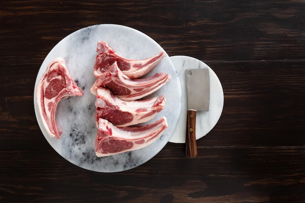 Cordero crudo fresco en las costillas en la placa de cocina de mármol de piedra sobre fondo de madera oscura.