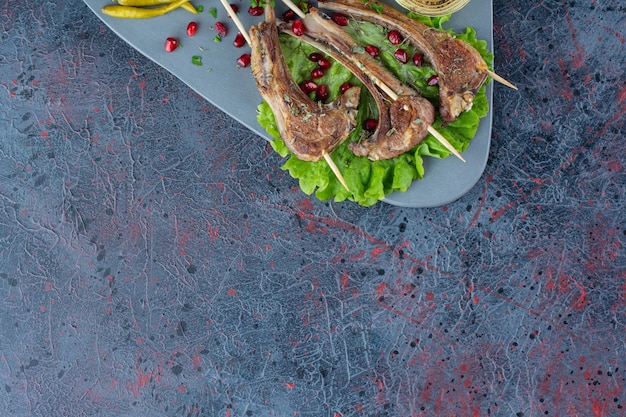 Corderos de carne a la brasa y verduras asadas en mesa de mármol.