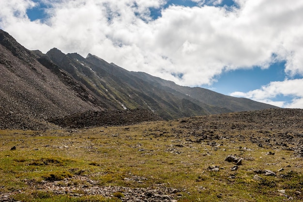 Cordillera y ladera de la montaña con piedras y hierba verde Cielo azul y nubes Horizontal