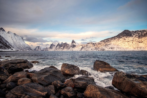 Cordillera nevada y olas golpeando la costa en invierno en la isla de Senja