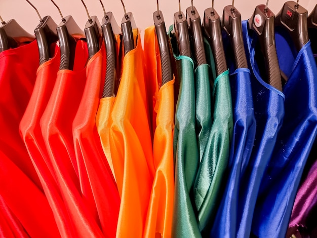 Cores do arco-íris. Escolha de roupas casuais em cabides pretos, isolados no branco. Variedade de vestidos de seda em cabides. Roupas coloridas penduradas no guarda-roupa