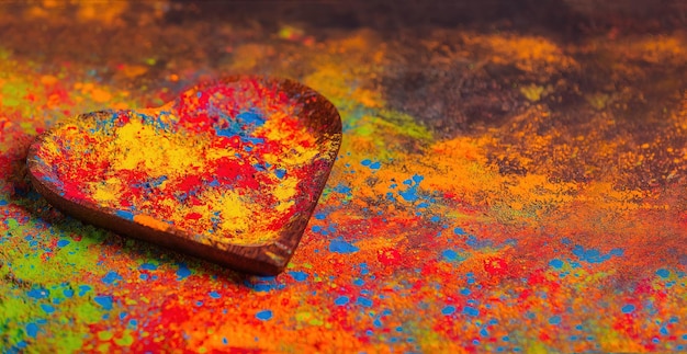 Cores Holi brilhantes multicoloridas orgânicas em placa de madeira em forma de coração em fundo escuro