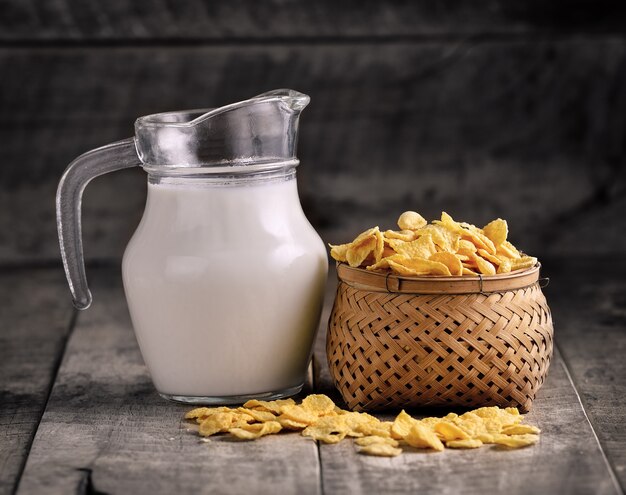 Cornflakes im Korb und im Glas Milch auf Holztisch