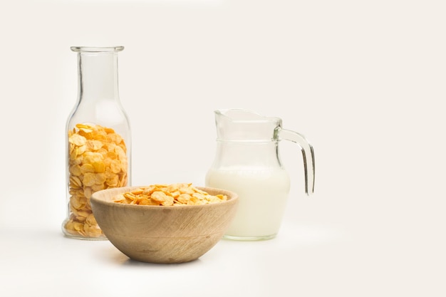 Cornflakes in einer Holzschale und in einer Flasche mit einem Glaskrug Milch auf weißem Hintergrund