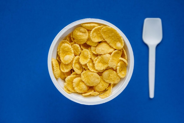 Cornflakes in weißer Schüssel mit Löffel auf blauem Hintergrund. Ansicht von oben. Kopieren, leerer Platz für Text