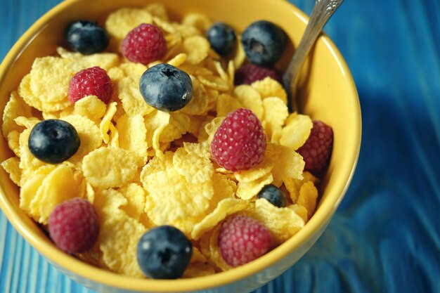 Cornflakes und verschiedene Beeren Blaubeeren und frische Himbeeren blauer Holzhintergrund