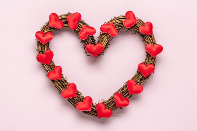 Coroa de vime em forma de coração decorada com corações vermelhos em fundo rosa