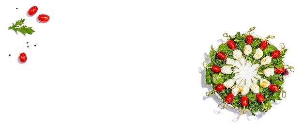 Corona de charcuterie aislada sobre fondo blanco Mozzarella tomates de cereza y rúcula en pinzas bocadillos de moda comida vegetariana festiva de moda fuerte luz oscura sombra