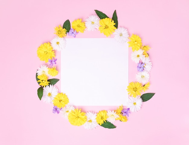 Foto corona creativa hecha con hermosas flores sobre fondo rosa pastel y tarjeta de felicitación blanca en blanco