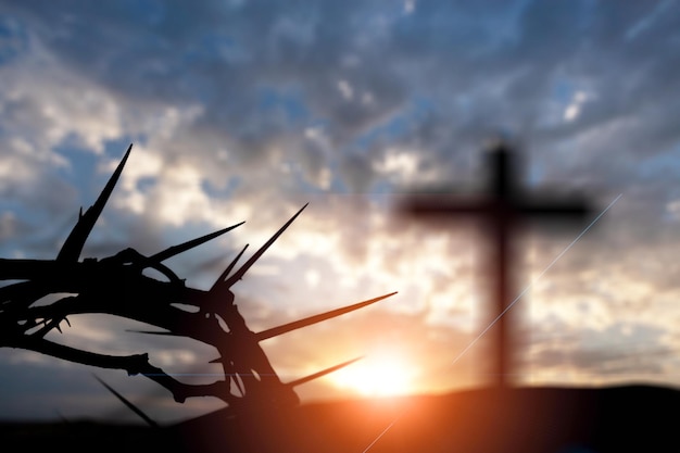 Corona de espinas de Jesucristo contra la cruz católica de madera al fondo de la puesta del sol