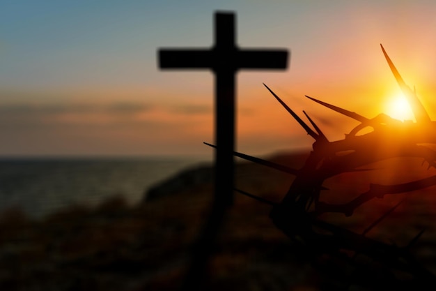 Corona de espinas de Jesucristo contra la cruz católica de madera en el fondo del atardecer