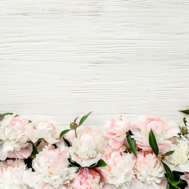 Corona de marco floral hecha de peonías rosas y beige capullos de flores ramas y hojas de eucalipto aisladas sobre fondo de madera blanca Vista plana superior