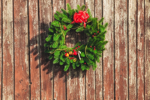 Corona de Navidad con adornos en la puerta de madera en mal estado.