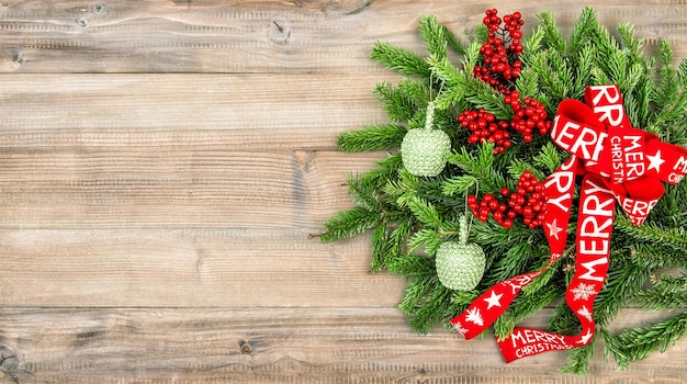 Corona de Navidad con cinta roja y adornos sobre fondo de madera. Decoración festiva. ¡Feliz Navidad!