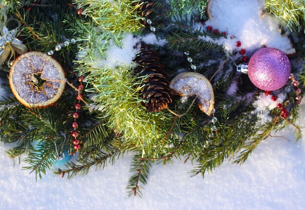 Corona de Navidad decorada con rodajas de naranja secas y bolas de colores sobre fondo blanco como la nieve.