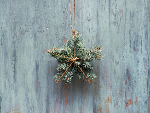 Corona de Navidad en forma de estrella dorada geométrica con ramas de abeto colgar en la puerta de madera rústica, adorno de Navidad tradicional.