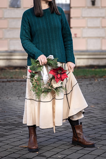 Corona de Navidad en manos de una mujer elegante a pie de la ciudad