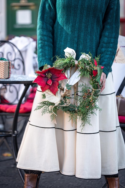 Corona de Navidad en manos de una mujer elegante a pie de la ciudad