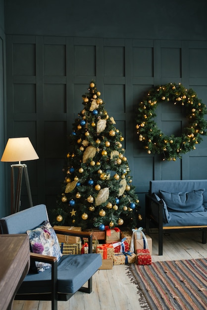 Corona de Navidad en la pared, abeto y sofá en la sala de estar con paredes azules