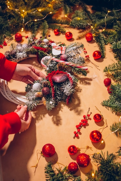 Corona de Navidad, Primer plano de manos femeninas hace una corona de abeto y decora con bolas rojas,