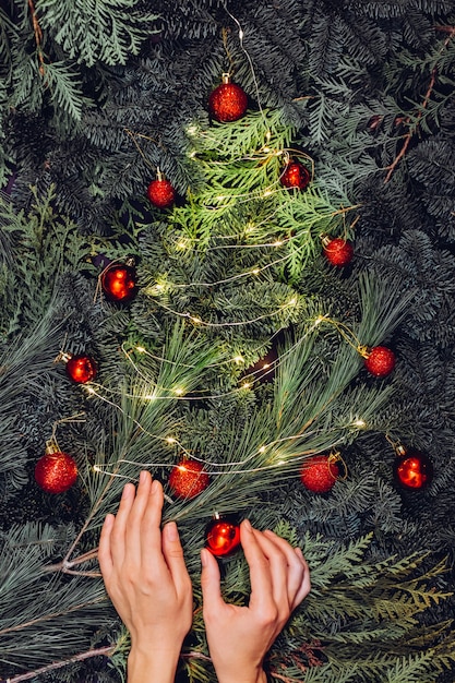 Foto corona de navidad, primer plano de manos femeninas hace una corona de abeto y decora con bolas rojas,