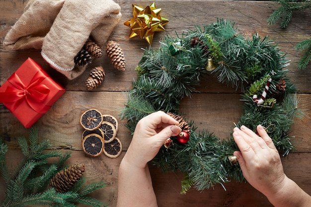 Corona de Navidad sobre fondo de madera. Manos de la abuela.