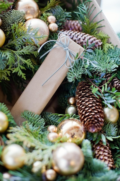 Corona navideña con elementos naturales, bolas navideñas doradas y regalo en envoltorio artesanal.