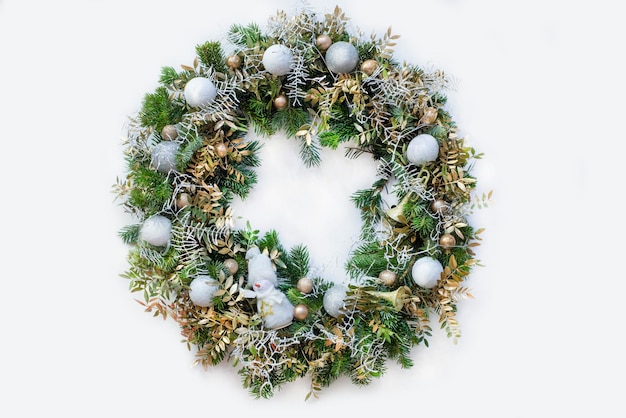 Corona navideña en la puerta de ramas de árboles de navidad decoradas con bolas de muñeco de nieve de juguete y blanco