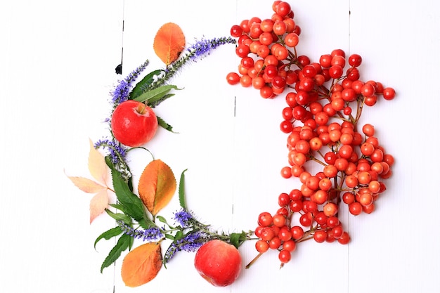 Corona de otoño decorado con bayas, frutas, hojas y flores sobre fondo de madera blanca vista desde arriba