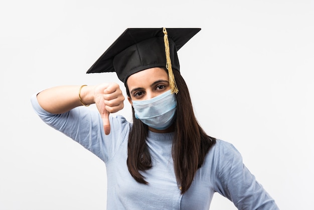 Corona Pandemia y confusión por los exámenes universitarios en India - Bonita estudiante india con expresiones confusas con mascarilla médica y sombrero de graduación
