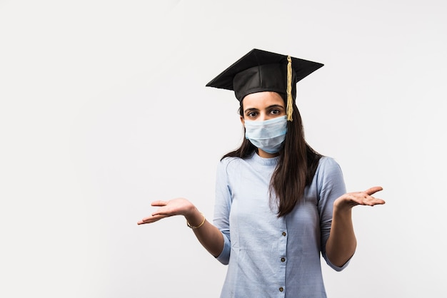 Corona Pandemia e confusão sobre os exames universitários na Índia - Linda estudante indiana com expressões confusas usando máscara médica e chapéu de formatura