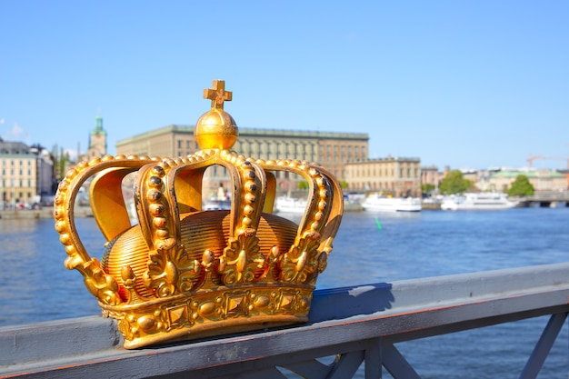 Corona sobre una barandilla de puente en Estocolmo y el Palacio Real en el fondo, Suecia