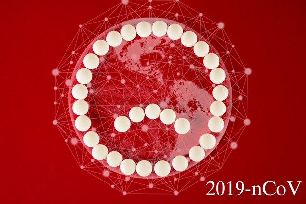 Coronavirus 2019-nCov neuartiges Coronavirus-Konzept, das für die asiatische Grippe, gefährliche Grippefälle Pandemie verantwortlich ist. Trauriges Smiley-Gesicht aus weißen Pillen und virtueller Hologrammerde auf rotem Hintergrund.
