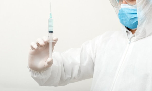 Coronavírus (COVID-19. Médico ou cientista em traje de proteção médico, risco biológico, máscara facial segurando a seringa com vacina no laboratório em branco