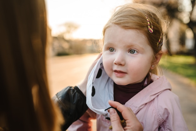 Coronavirus das Endkonzept. Nie mehr covid-19. Kleines Mädchen, Mutter tragen Masken gehen auf der Straße. Mutter entfernt Maske glückliches Kind. Familie mit Kind im Freien. Erfolg feiern. Die Pandemie ist vorbei, ist beendet.