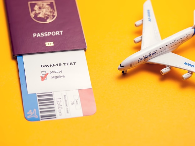 Coronavírus e conceito de viagens seguras, teste Covid-19 com marca "Negativa", passagem aérea, passaporte e avião em fundo amarelo