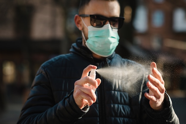 Coronavirus. Hände mit Desinfektionsspray in der Stadt reinigen. Mann, der in der medizinischen Schutzmaske auf Straße trägt. Desinfektionsmittel zur Vorbeugung von Coronavirus, Covid-19, Grippe. Sprühflasche. Viren- und Krankheitsschutz.