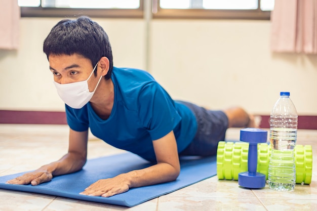 Coronavirus, un hombre asiático usa una máscara y hace ejercicio solo en la habitación de su casa para prevenir Covid-19. Entrenamiento desde casa, ejercicio desde casa.