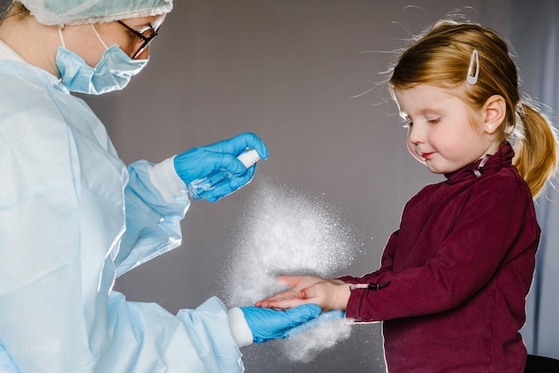 Coronavirus. Krankenschwester oder Arzt in einem Schutzanzug, Maske sagt Kind, wie man das Desinfektionsmittel verwendet. Vorbeugende Maßnahmen gegen Covid-19-Infektion. Antibakterielles Gel mit Handwaschspray auf Alkoholbasis.