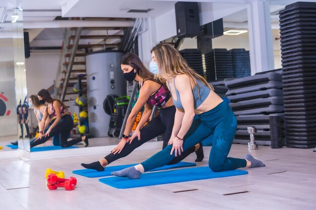 Coronavirus-Pandemie in Fitnessstudios Zwei Mädchen dehnen sich mit Gesichtsmasken