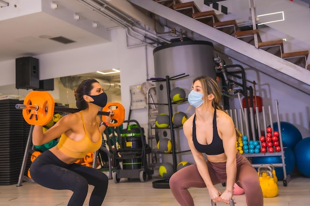 Coronavirus-Pandemie in Fitnessstudios Zwei Mädchen trainieren mit Gewichten mit Gesichtsmasken