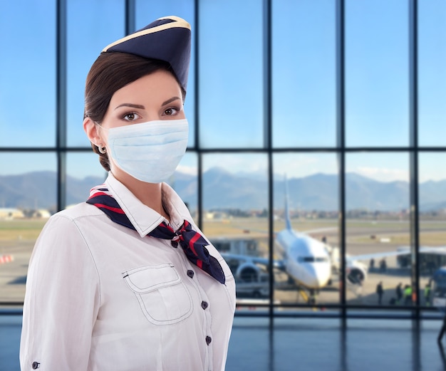 Coronavirus-Pandemie-Urlaubs- und Reisekonzept-Stewardess in Maske, die im Flughafen posiert