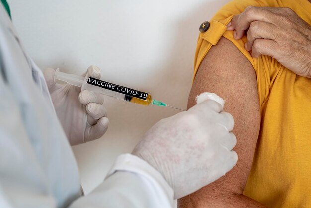 Coronavirus. Primer plano de una jeringa que contiene la vacuna contra el coronavirus covid-19, un médico se la inyecta a una anciana con una camisa amarilla