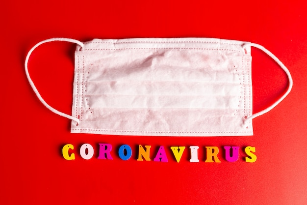 Coronavirus-Wort aus bunten Buchstaben auf rotem Hintergrund. Die Inschrift auf der medizinischen Schutzmaske Coronavirus.