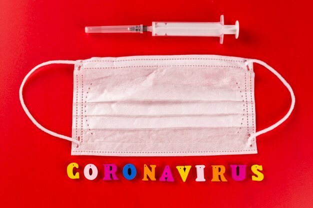 Coronavirus-Wort aus bunten Buchstaben auf rotem Hintergrund. Die Inschrift auf der medizinischen Schutzmaske Coronavirus.