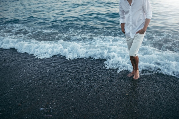 Corpo de homem cortado atraente vestindo camisa branca e calça na praia e mar vista frontal de fundo ao ar livre Viagem férias férias Homem andando descalço no mar ao pôr do sol no fundo