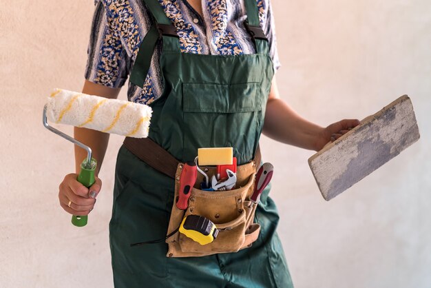 Corpo feminino de uniforme com cinto de ferramentas e equipamento de pintura