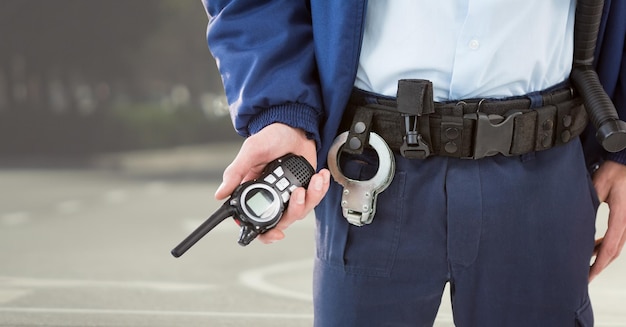 Corpo inferior do guarda de segurança com walkie talkie contra a rua embaçada